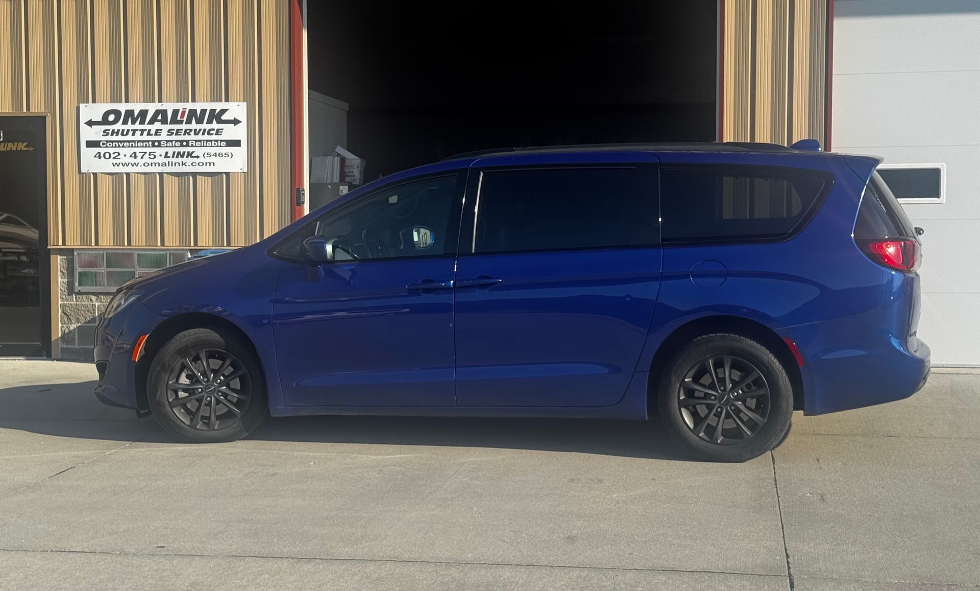 A blue Chrysler Pacifica minivan parked on a concrete lot in front of a building.