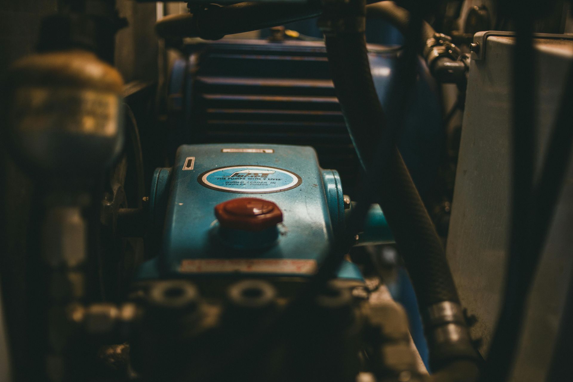 Close-up of a blue engine component with a red cap inside a dimly lit machine compartment