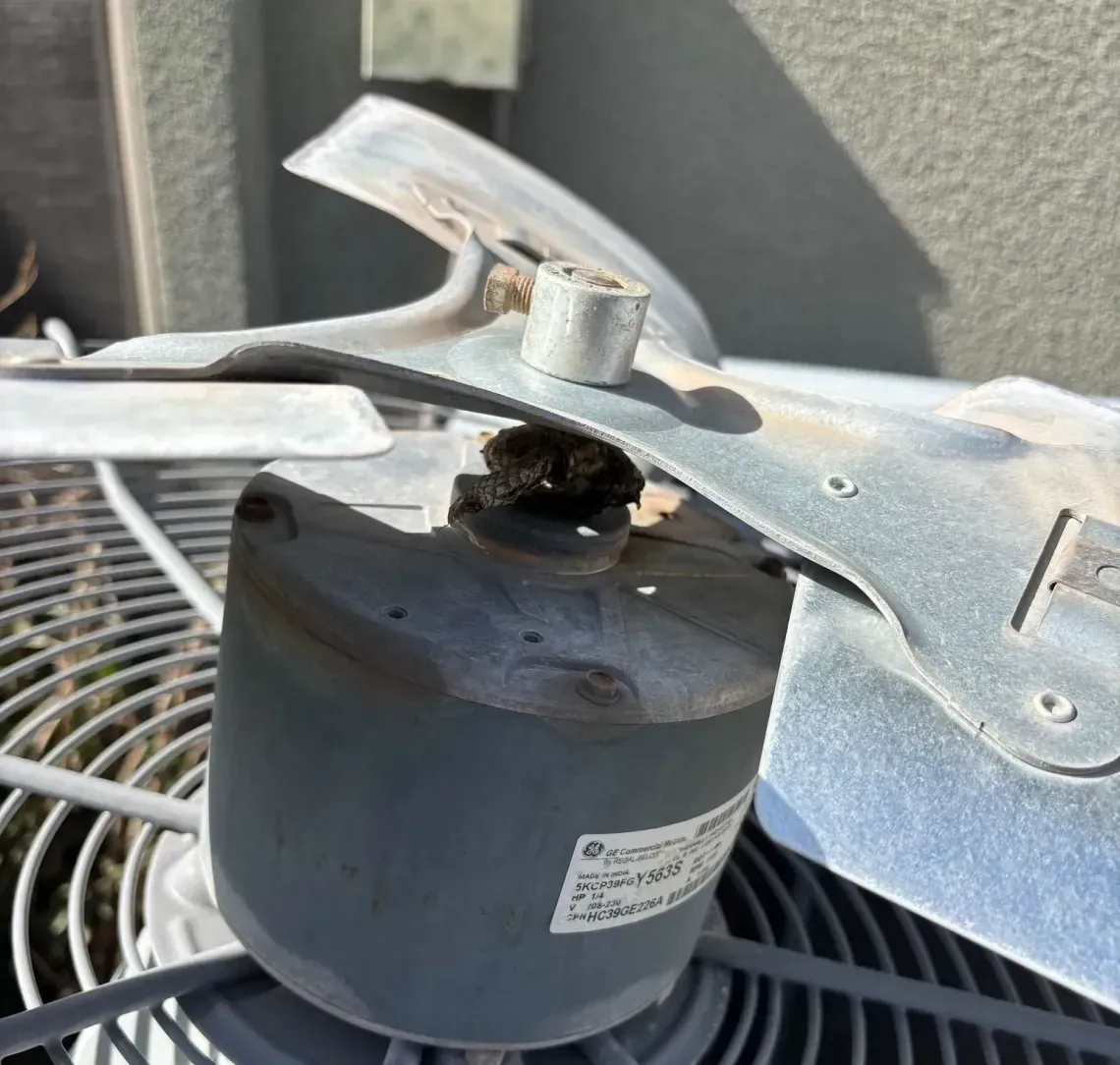 Close-up of a dusty outdoor fan motor and blades on an air conditioning unit.