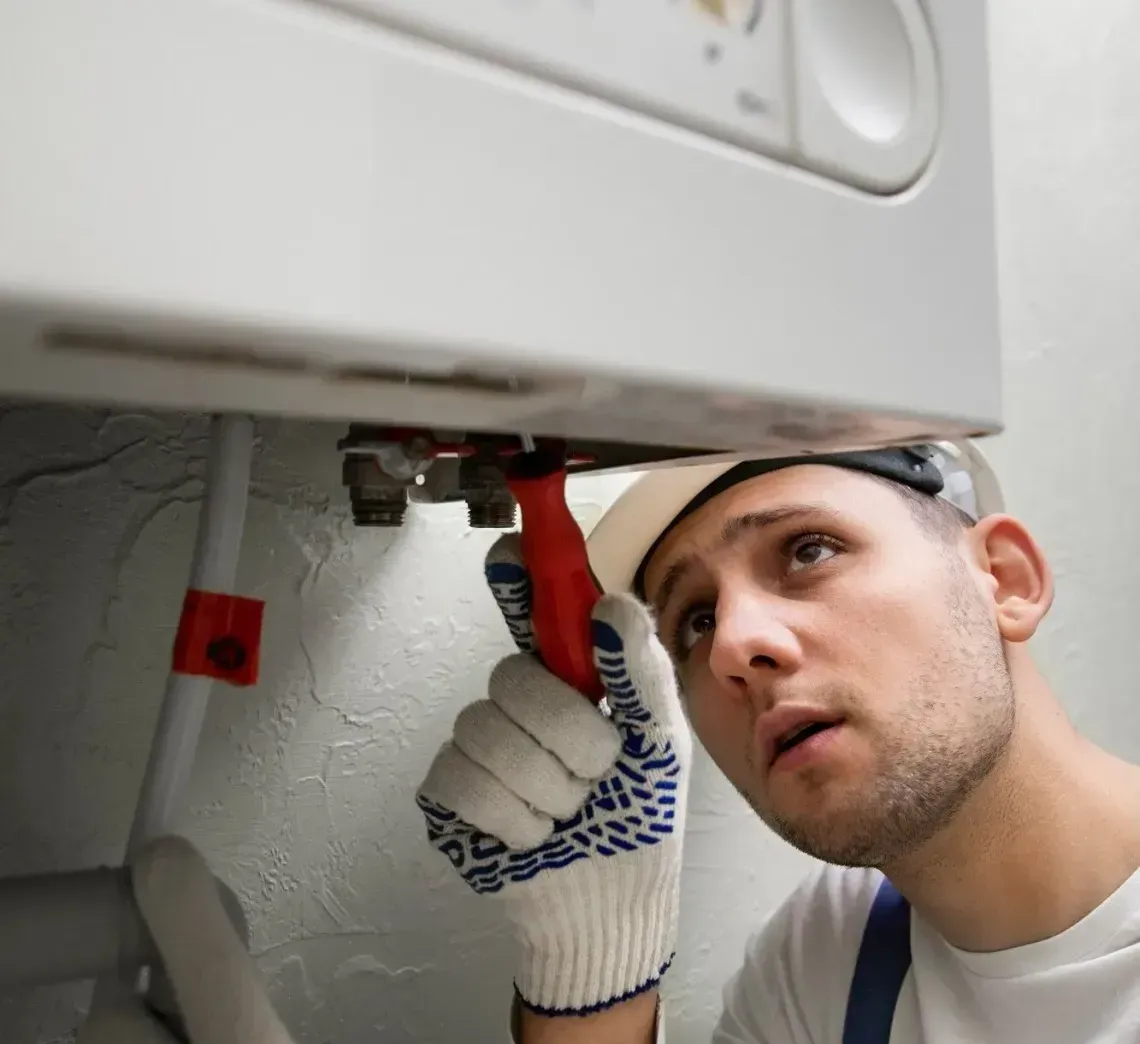 Technician repairing plumbing under a sink, using a wrench in a small bathroom cabinet.