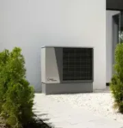 Outdoor HVAC unit beside a white house, surrounded by gravel and green shrubs.