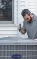 Technician inspecting a home air conditioner unit outside a house