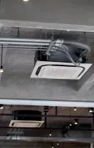 Two outdoor HVAC units on gravel beside a wooden fence and brick wall