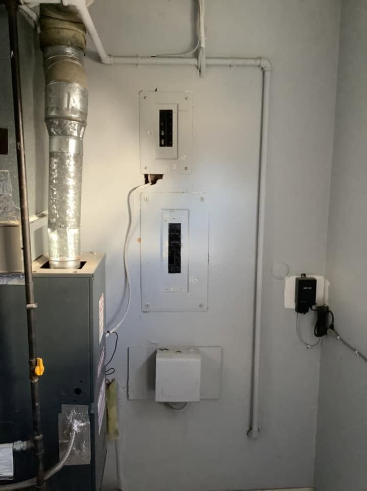 Utility room wall with breaker panels, exposed ductwork, and electrical wiring.