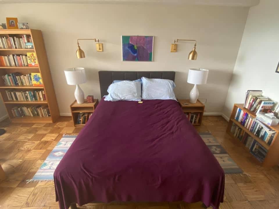 Bedroom with a purple bedspread, white pillows, bedside lamps, and bookshelves on both sides.