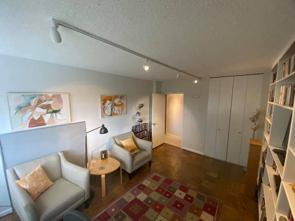 Cozy living room with two armchairs, patterned rug, floor lamp, wall art, bookshelves, and white storage cabinets.