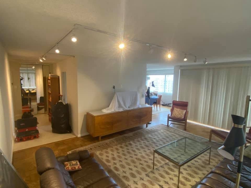 Bright living room with sofa, glass coffee table, TV stand, and open dining area with curtains.