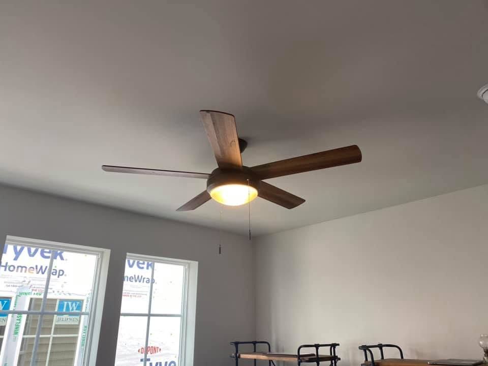 Bright room with white walls, ceiling fan light, and windows with stacked chairs by the wall