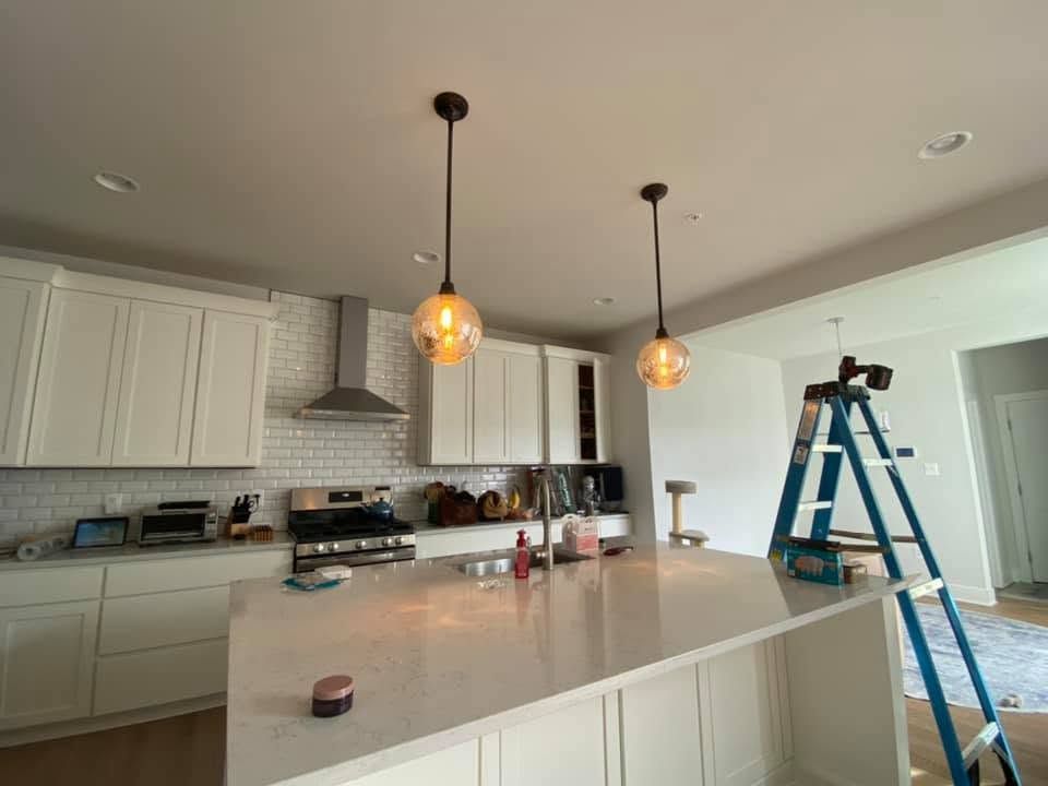 Bright kitchen with white cabinets, island, hanging pendant lights, and a blue ladder during renovation