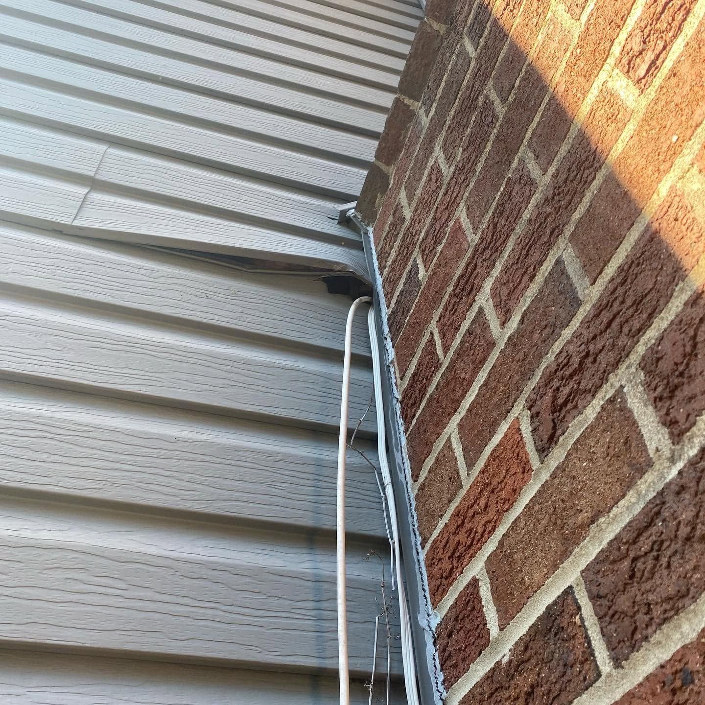 White siding and red brick wall with exposed cables at a building corner