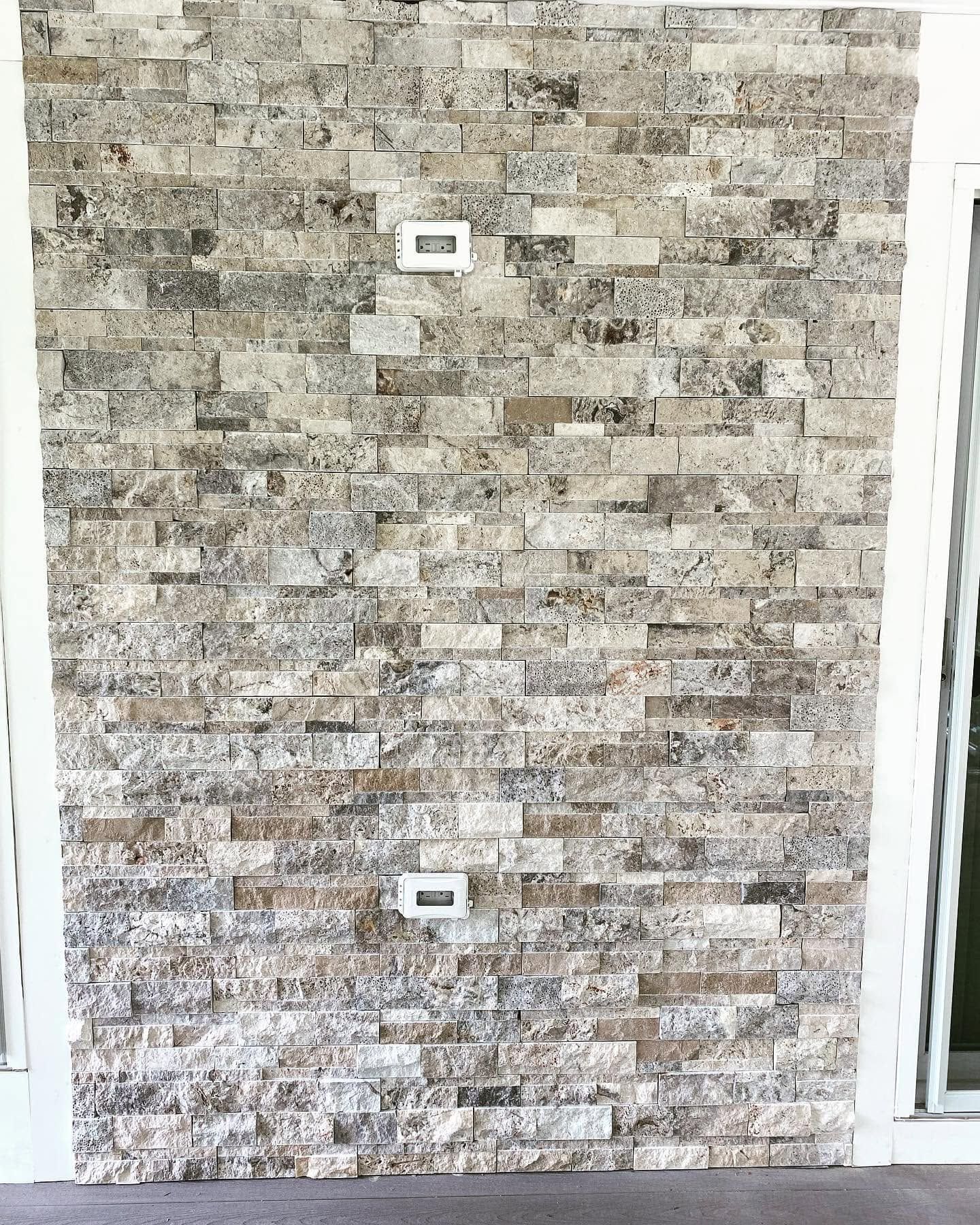 Stone-tile wall with two electrical outlets and a glass door frame on the right