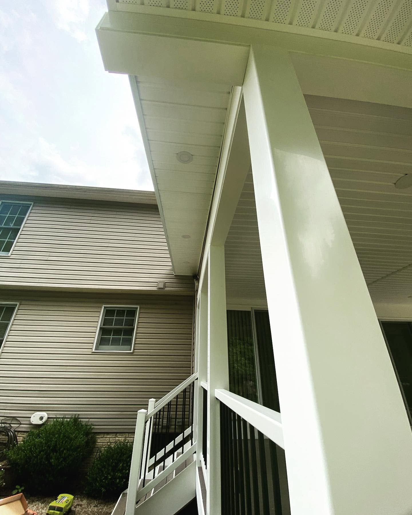 White porch columns and railing beside a beige house under a covered roof.