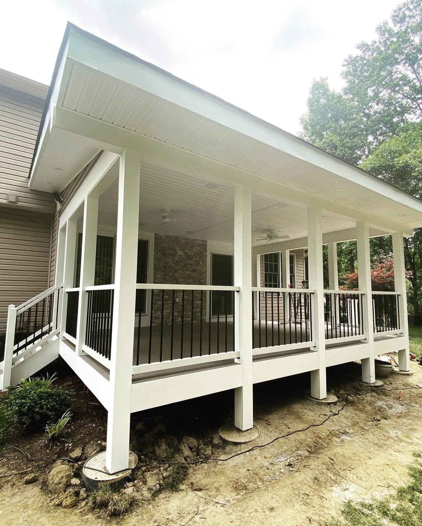 White screened porch with sloped roof and black railing elevated on posts beside a wooded yard