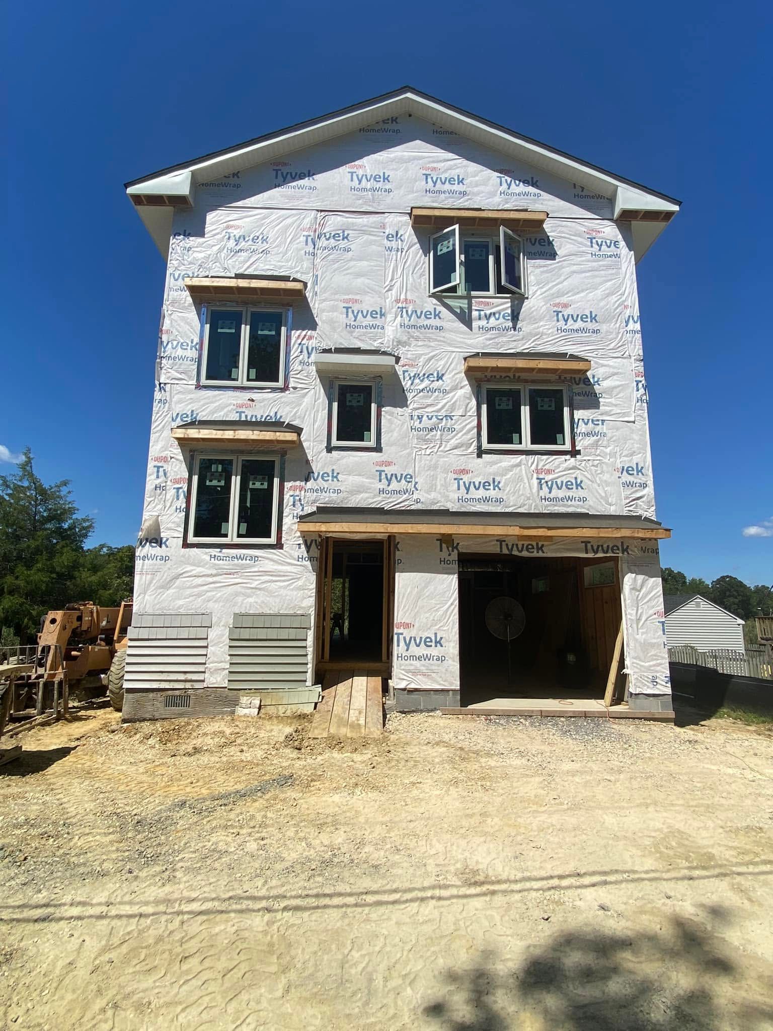 Three-story house under construction with white stone exterior and open garage on a sunny day