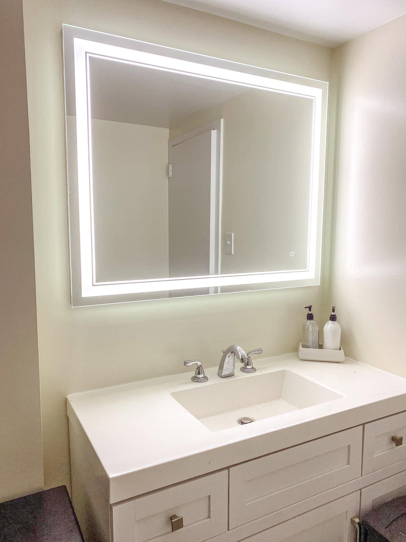 Bright bathroom vanity with a lit mirror, white countertop, sink, and faucet.