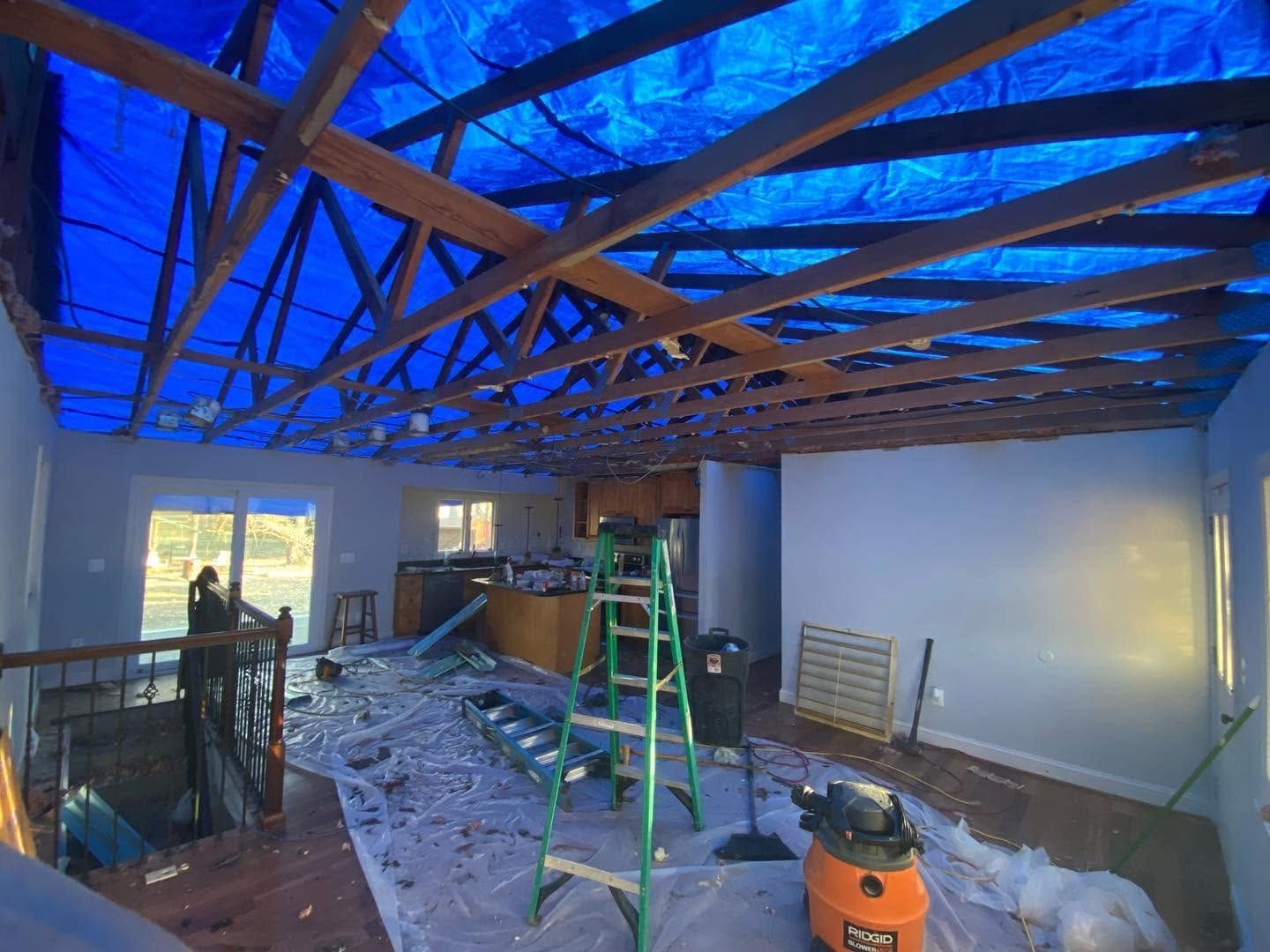 Interior under renovation with exposed wooden roof beams, ladder, debris, and construction equipment