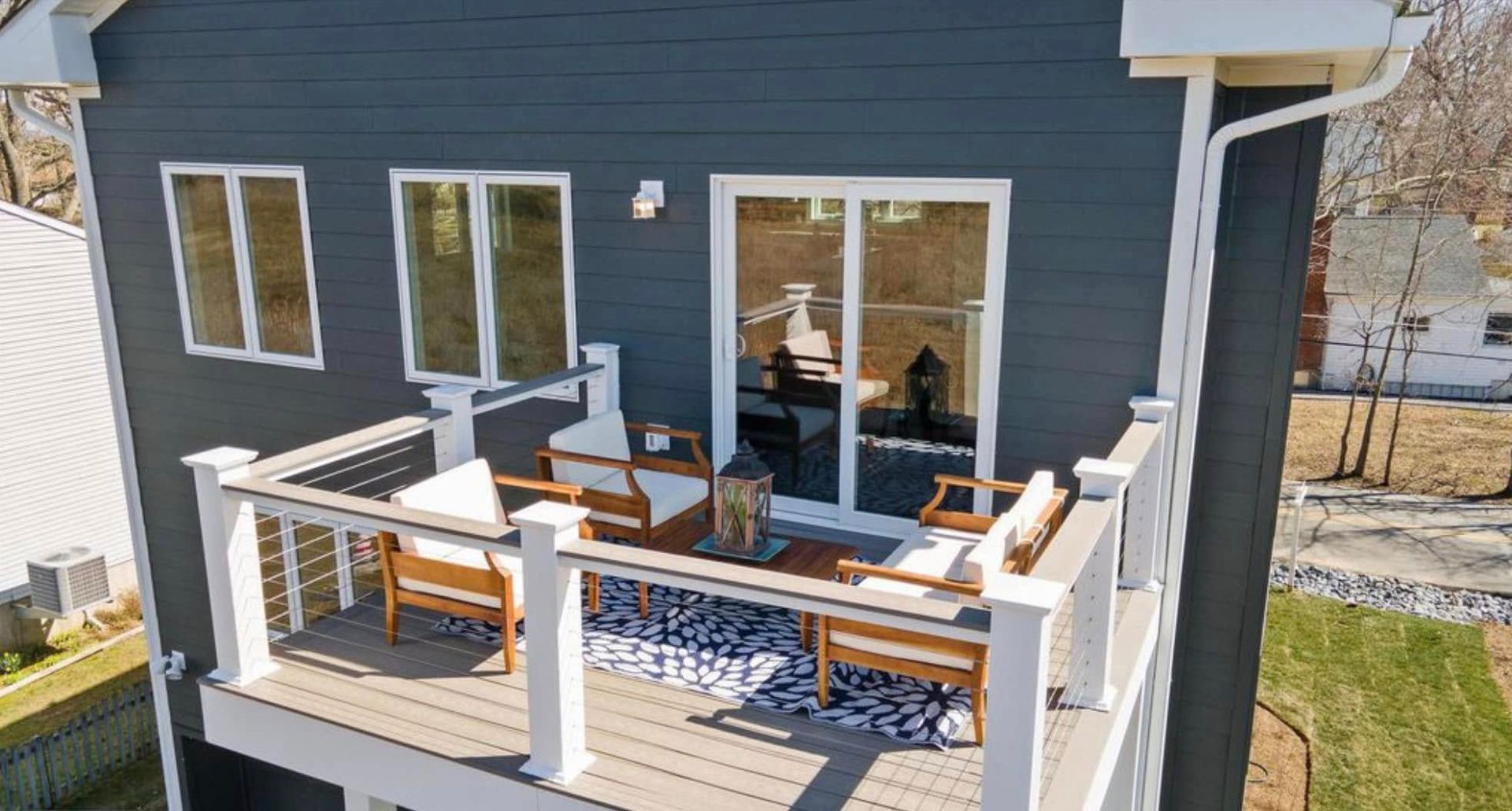 Back deck with white railing, outdoor seating, and sliding glass doors on a blue house