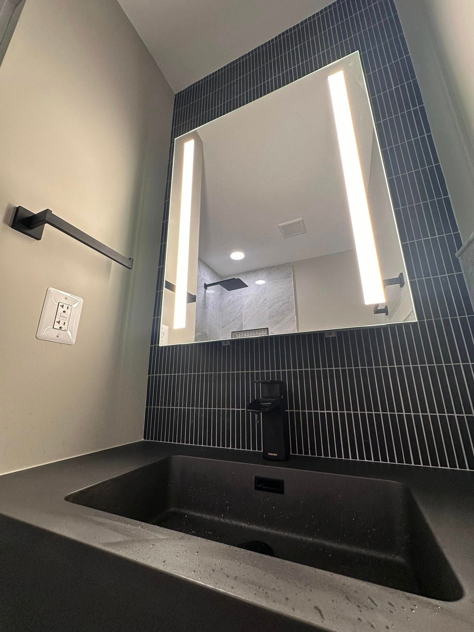 Modern bathroom vanity with black sink, illuminated mirror, and patterned tile wall