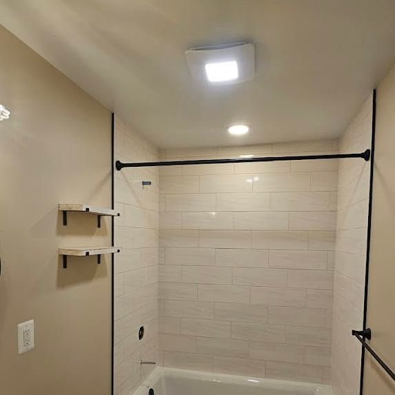 Small beige bathroom with a white tiled shower stall, shower curtain rod, and ceiling light.