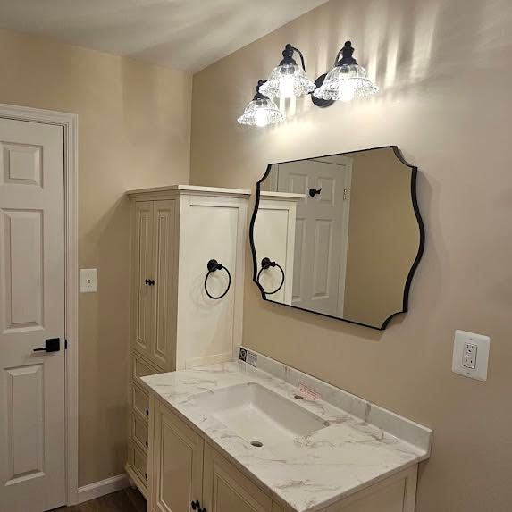 Bathroom vanity with beige cabinets, white countertop, mirror, and wall lights against tan walls