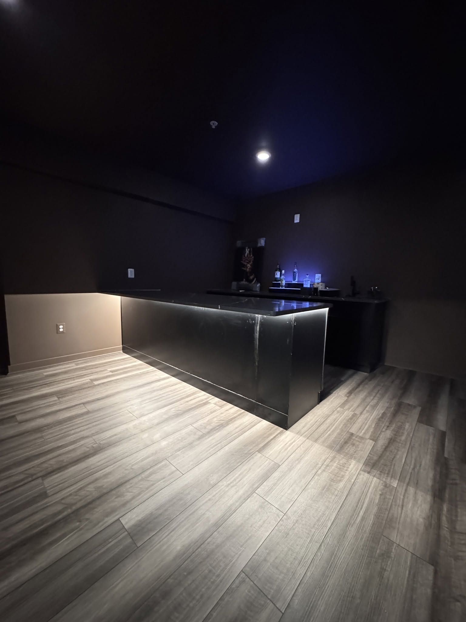Dark modern kitchen with black cabinets, wood flooring, pendant light, and a glowing stove area