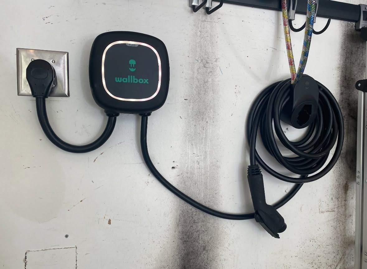 Wall-mounted EV charger with coiled cable beside an electrical outlet on a white wall