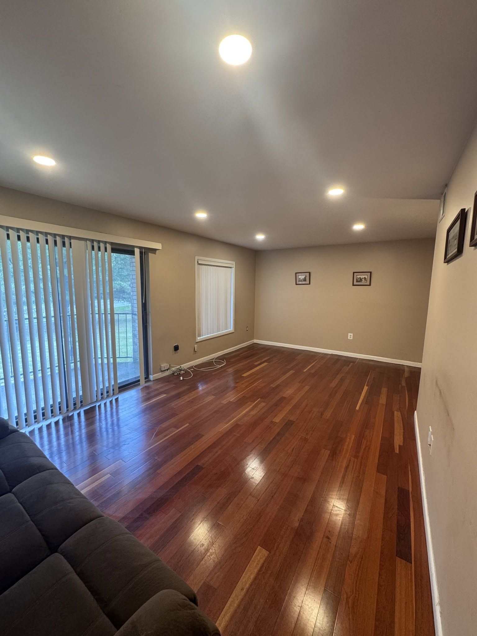 Empty living room with hardwood floors, recessed lights, sliding glass door, and beige walls