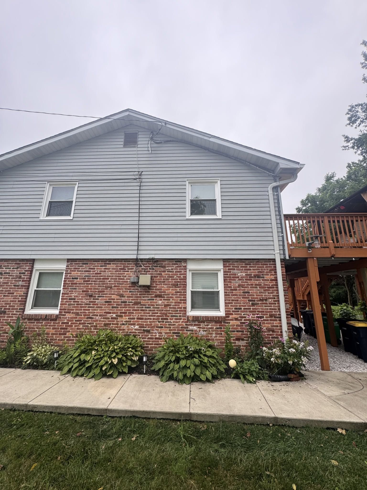 Two-story house with gray siding, red brick lower level, white trim, and a wooden deck on the right.