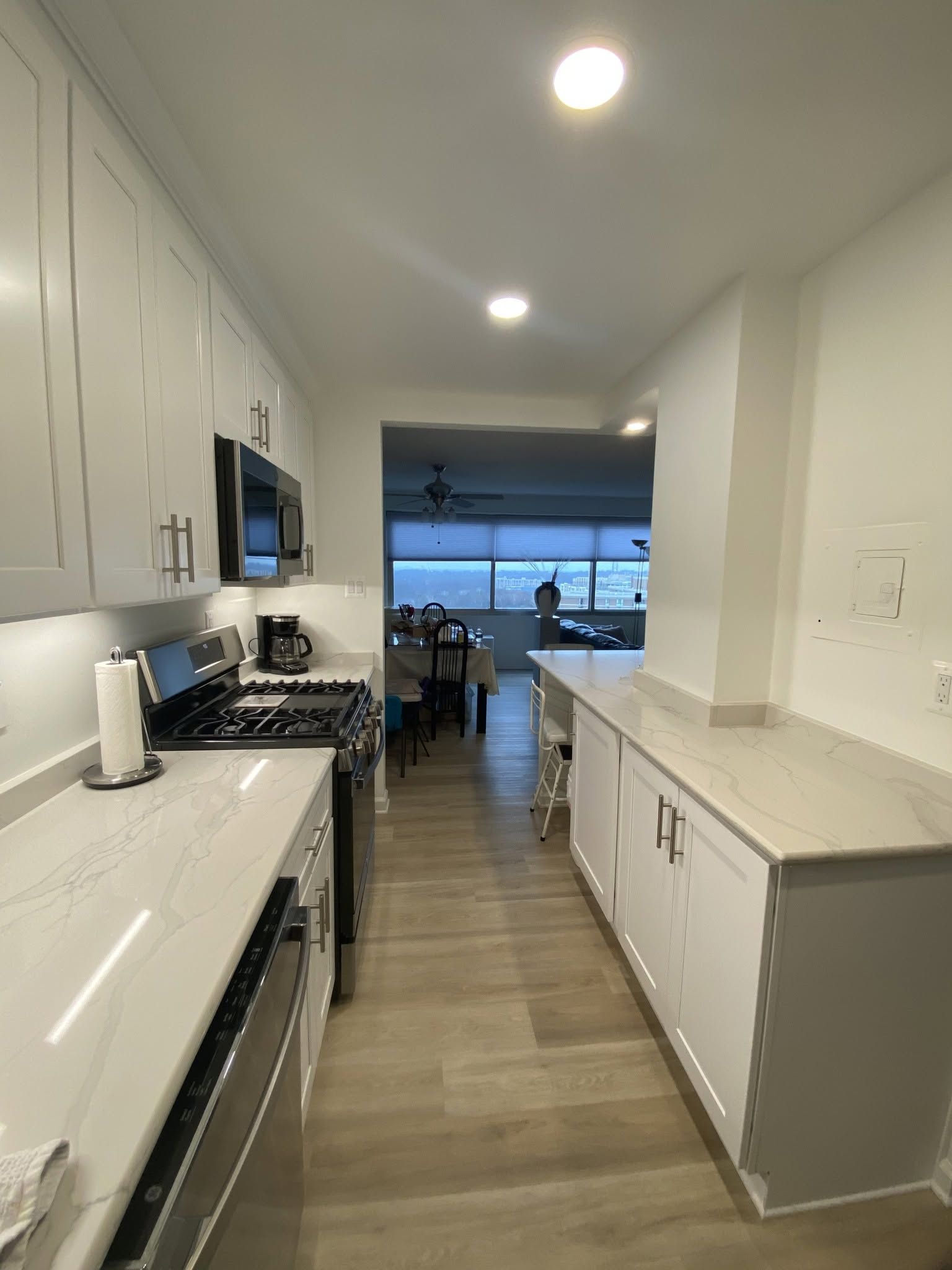 Bright modern kitchen with white cabinets, gray countertops, and a view into a dining area and ocean beyond.