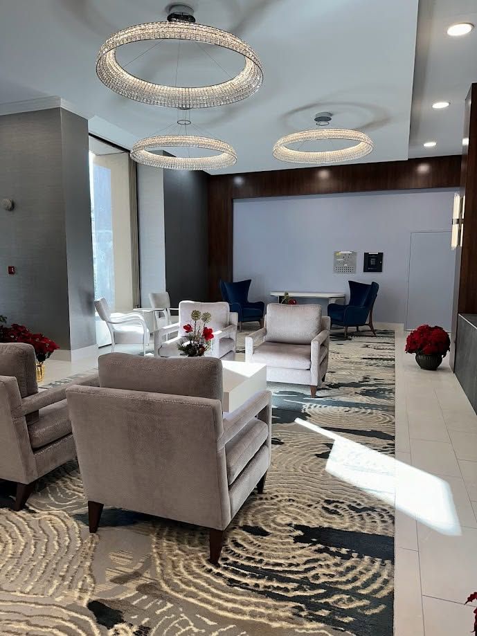 Modern lounge with beige chairs, patterned rug, circular chandeliers, and a small table in a bright hallway
