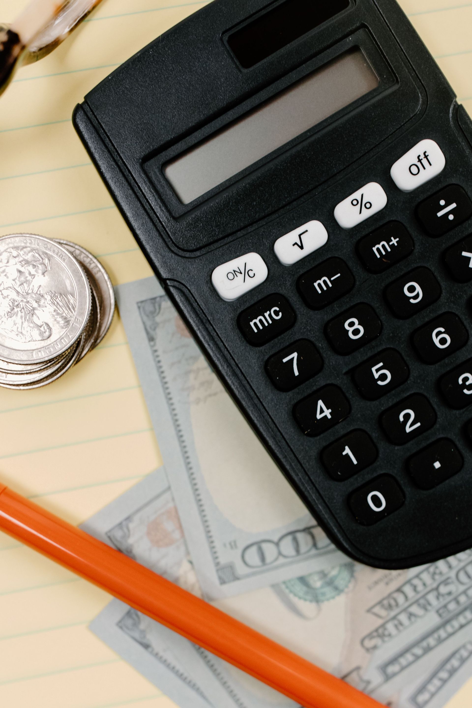 Calculator, cash, and coin on a notepad with an orange pencil