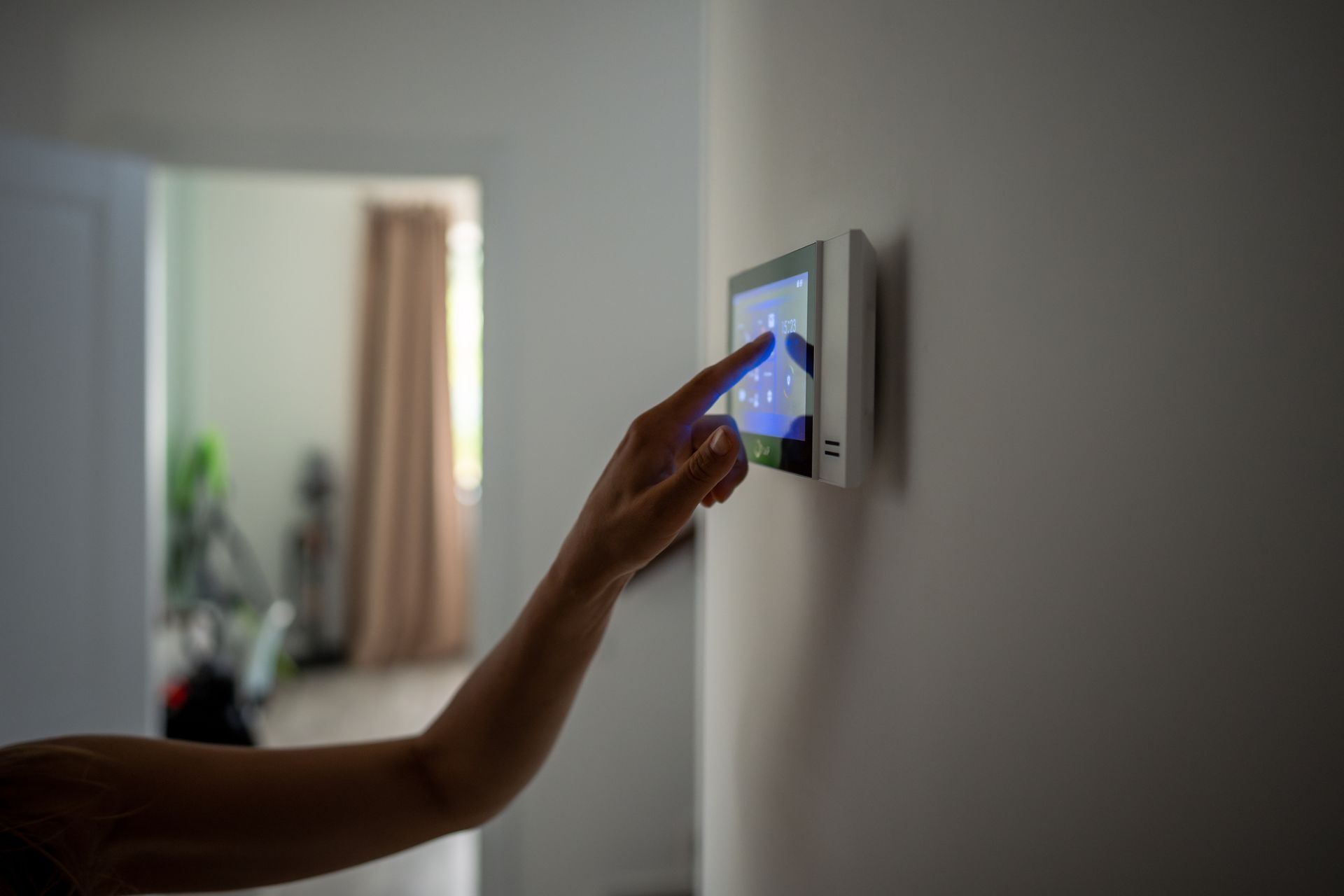 Hand reaching a wall-mounted touchscreen thermostat in a softly lit room