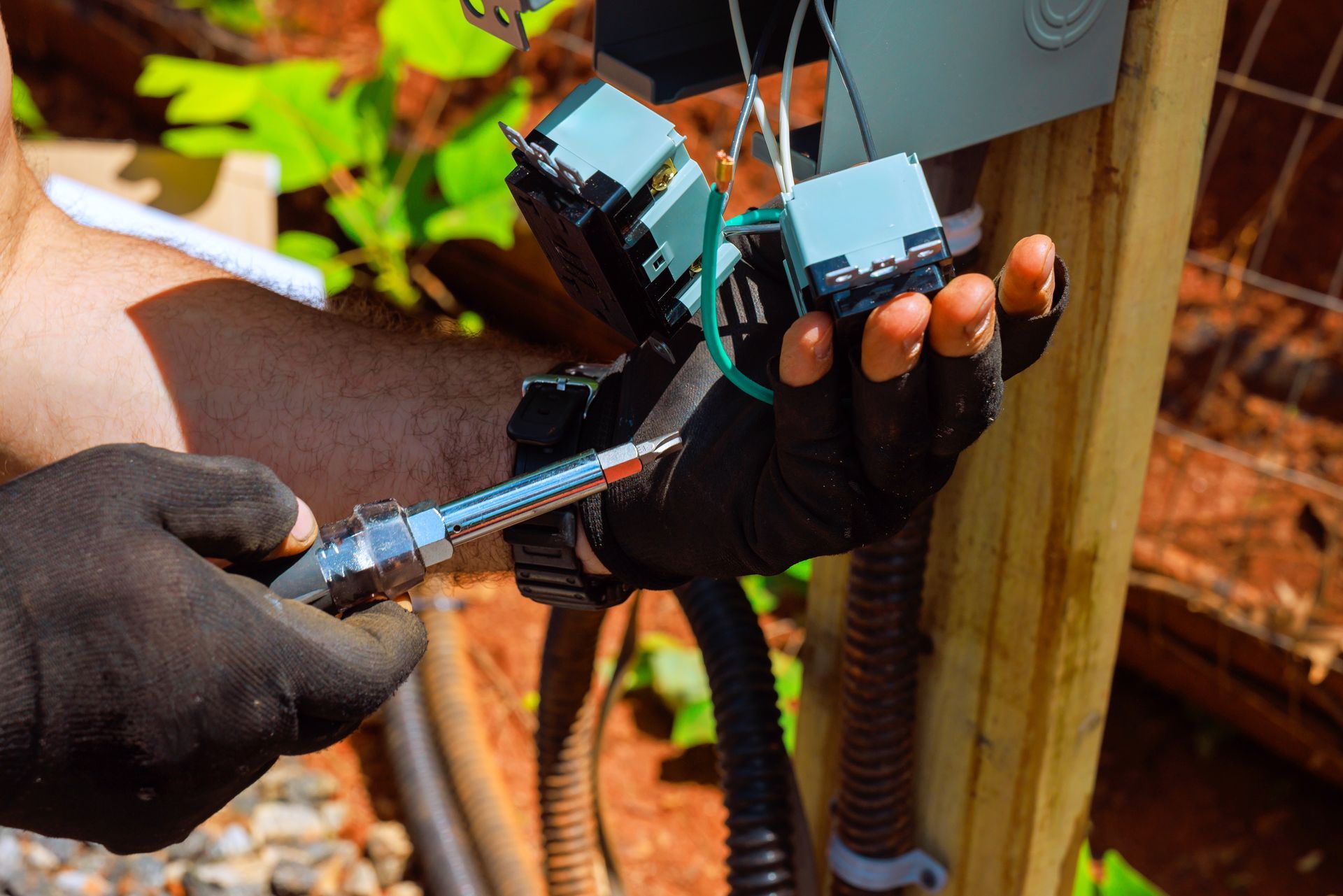 Gloved hands connecting an electrical cable to a gray outdoor control box