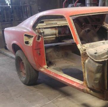 Red, gutted classic car body in a workshop, undergoing restoration.