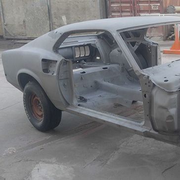 A gray, stripped-down classic muscle car body, possibly undergoing restoration, outdoors.