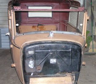 Tan and maroon antique car body, front view; missing engine, windows, and seats.