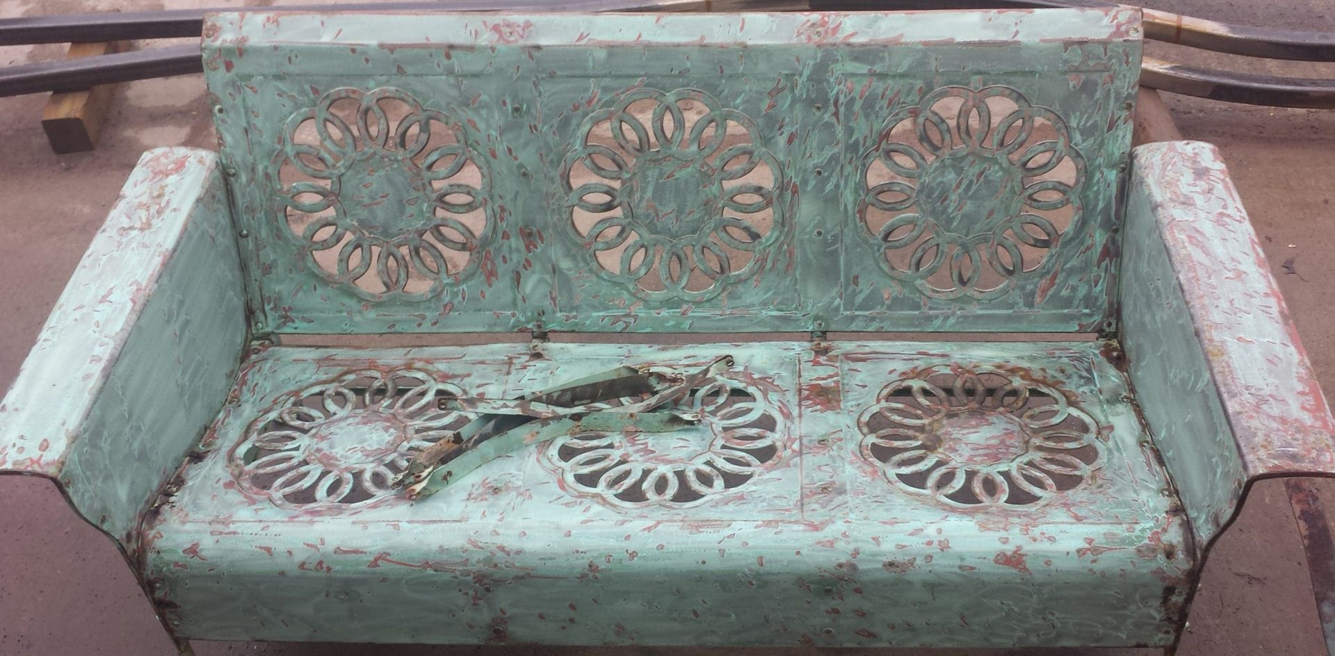 Weathered teal metal bench with decorative circular cutouts.