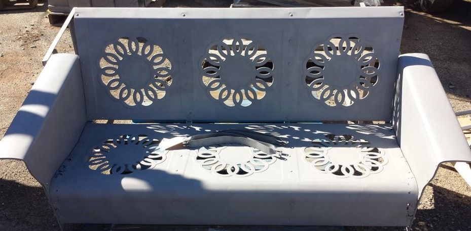 Metal bench with floral cutouts in the back and seat, painted gray.