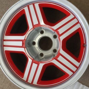 Red and white multi-spoke car wheel with a silver center hub, set against a white rim.