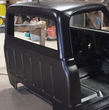 Black truck cab and bed, freshly painted, interior visible, shop setting.
