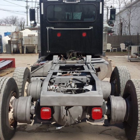 Rear view of a black semi-truck cab, showing the chassis, wheels, and taillights in an outdoor setting.