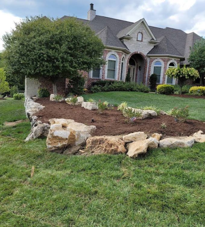 Front yard landscaping with stone-bordered mulch bed and a brick house in the background