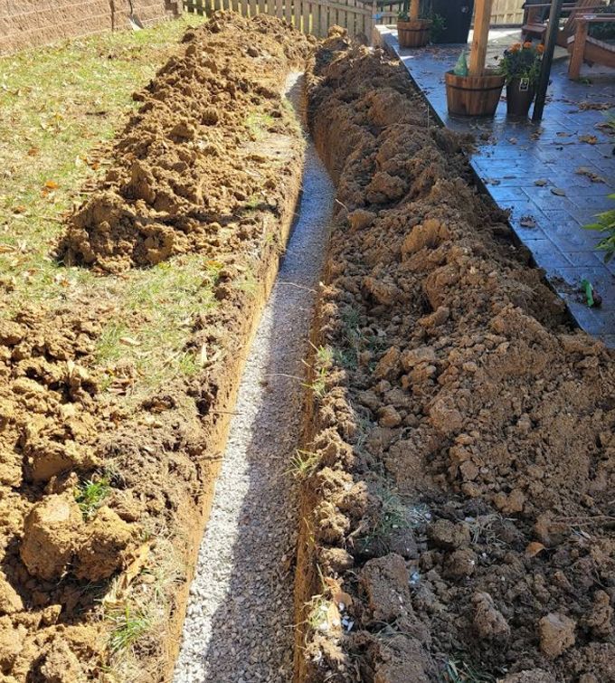 Freshly dug trench beside a patio, with piles of soil lining both sides
