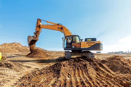 Excavator digging earth at a construction site under a clear blue sky