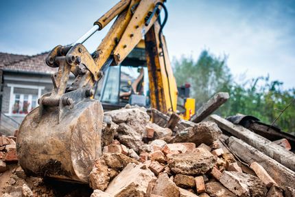 Yellow excavator clearing rubble at a demolition site