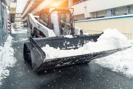 Snowplow clearing snow from a street, with snow piled in its front bucket.