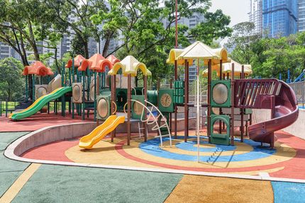 Colorful outdoor playground with slides, climbing structures, and rubber safety flooring in a park.