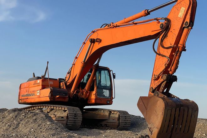 Orange excavator on a gravel lot with its bucket raised against a clear sky