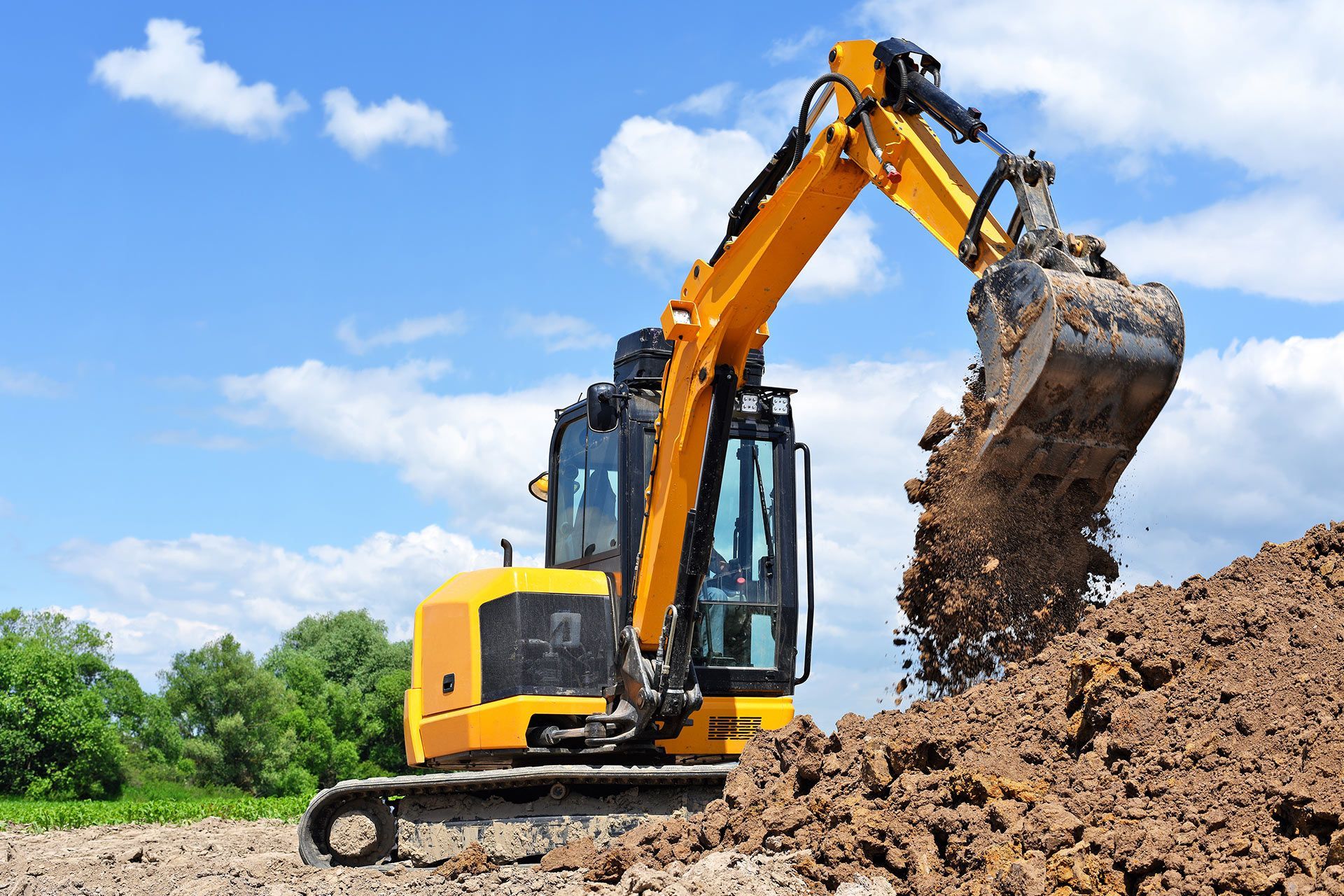 Yellow excavator digging dirt at a construction site under a blue sky
