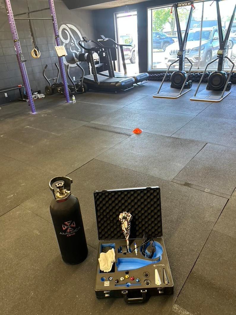 Gym floor with a water bottle and open workout kit in the foreground, equipment and medicine ball in the background